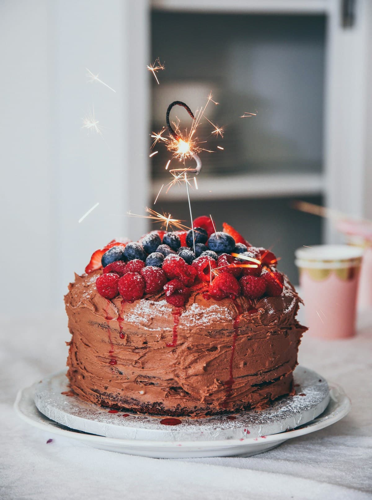 Torta de chocolate cubierta de frambuesas y arándanos, con un chispero encendido