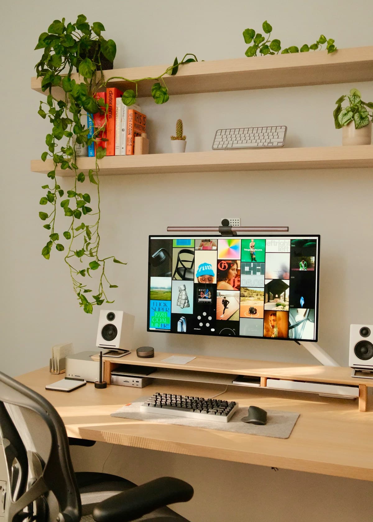 Escritorio de madera con monitor, teclado y dos parlantes pequeños, con plantas colgando de un estante